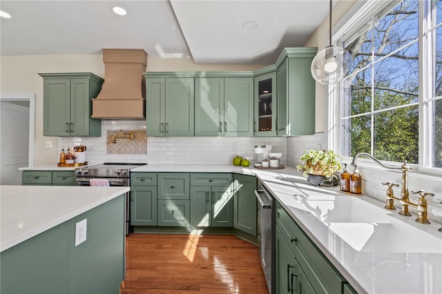 kitchen with glass insert cabinets, hanging light fixtures, custom exhaust hood, light countertops, and green cabinetry