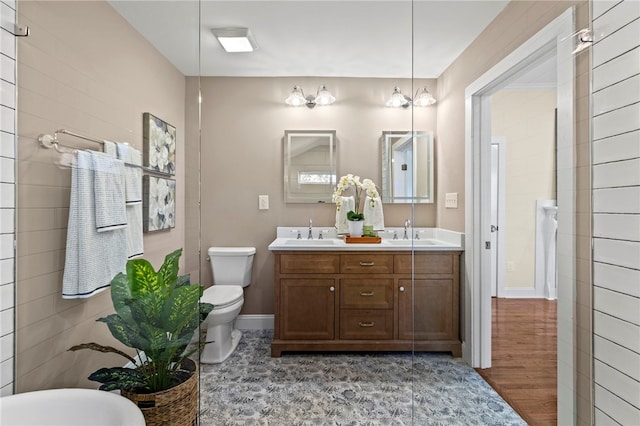 full bathroom featuring double vanity, a sink, toilet, and baseboards