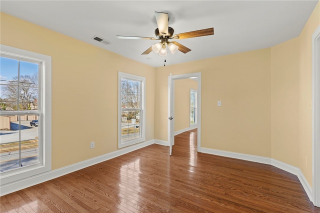 empty room with baseboards, visible vents, plenty of natural light, and hardwood / wood-style floors