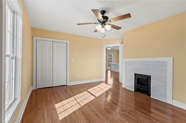 unfurnished living room with a ceiling fan, a fireplace, baseboards, and wood finished floors