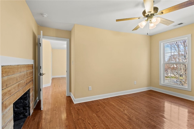 spare room featuring a fireplace, wood finished floors, a ceiling fan, visible vents, and baseboards