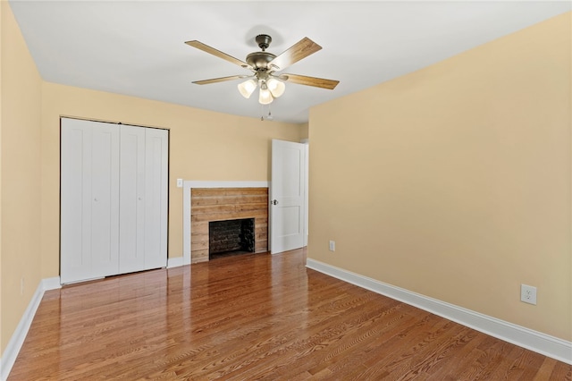 unfurnished bedroom with baseboards, a ceiling fan, wood finished floors, a fireplace, and a closet