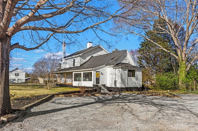 view of front facade with driveway, a chimney, and roof with shingles