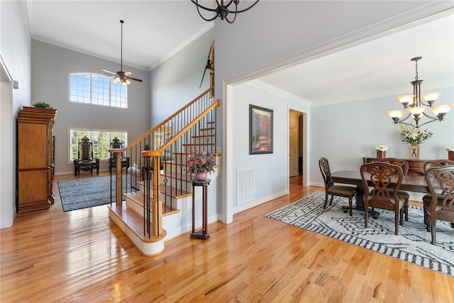 dining area featuring light wood-type flooring, ornamental molding, ceiling fan with notable chandelier, and a high ceiling