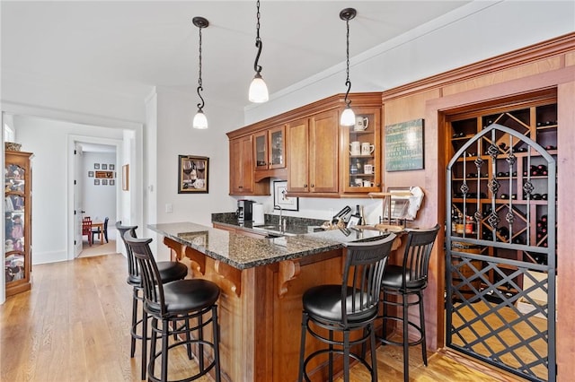 kitchen with decorative light fixtures, a kitchen bar, dark stone counters, light hardwood / wood-style floors, and kitchen peninsula