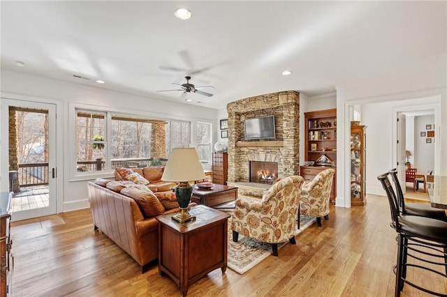 living room with ceiling fan, a stone fireplace, and light wood-type flooring