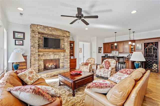 living room with ceiling fan, light hardwood / wood-style floors, and a stone fireplace