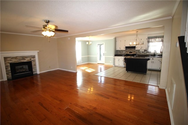 unfurnished living room featuring light wood-type flooring, a fireplace, crown molding, and ceiling fan with notable chandelier