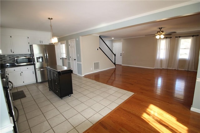 kitchen featuring ceiling fan, appliances with stainless steel finishes, decorative backsplash, white cabinets, and a center island