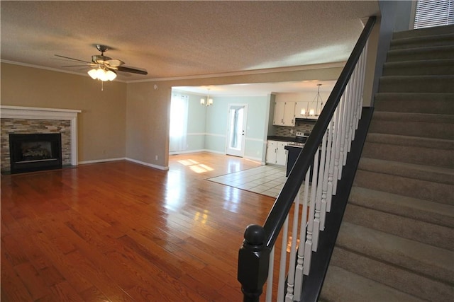 unfurnished living room featuring a textured ceiling, a fireplace, light hardwood / wood-style floors, ornamental molding, and ceiling fan