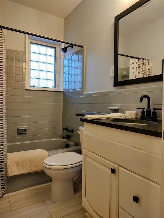 full bathroom with tile walls, shower / bath combination with curtain, decorative backsplash, vanity, and toilet