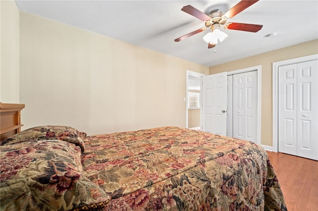 bedroom with ceiling fan, multiple closets, and light hardwood / wood-style flooring