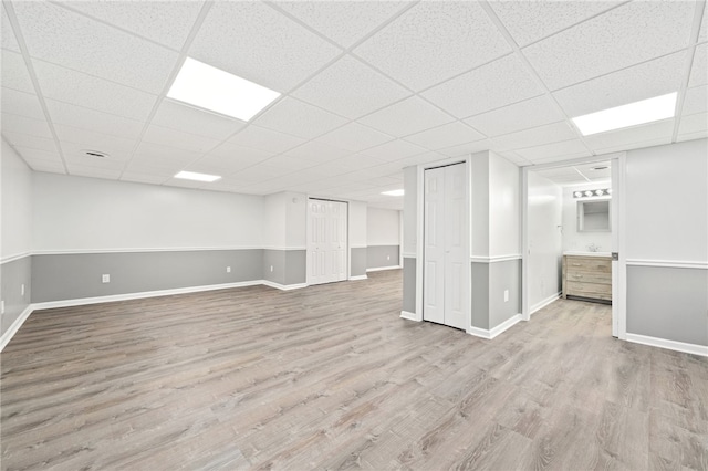 basement featuring a drop ceiling and light hardwood / wood-style flooring