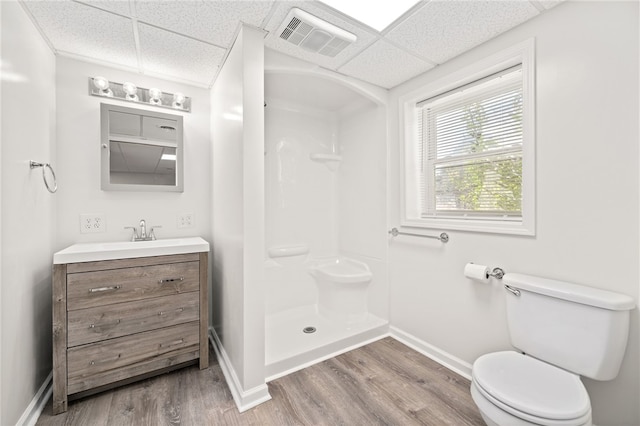 bathroom with hardwood / wood-style flooring, a shower, toilet, and a paneled ceiling