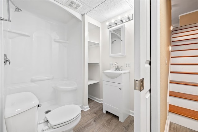 bathroom with hardwood / wood-style floors, a paneled ceiling, vanity, toilet, and walk in shower