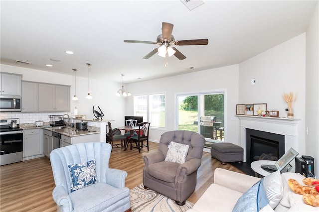 living room featuring ceiling fan with notable chandelier, sink, and light hardwood / wood-style floors