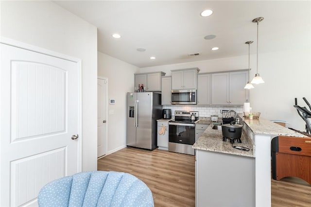 kitchen with kitchen peninsula, gray cabinets, stainless steel appliances, pendant lighting, and light stone counters