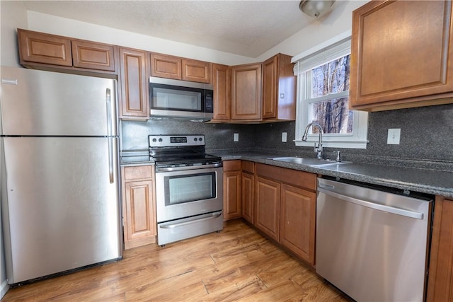 kitchen featuring appliances with stainless steel finishes, decorative backsplash, dark stone counters, light hardwood / wood-style flooring, and sink