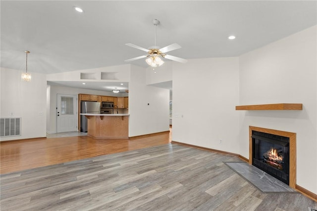 unfurnished living room with ceiling fan, lofted ceiling, and light wood-type flooring