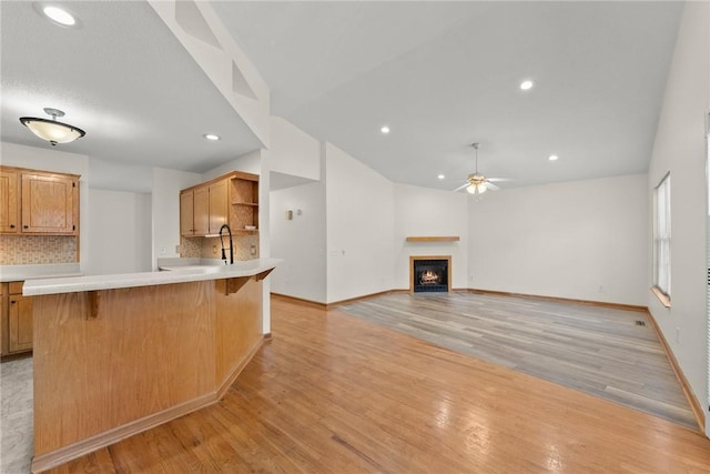 kitchen featuring a breakfast bar area, ceiling fan, tasteful backsplash, light hardwood / wood-style flooring, and sink