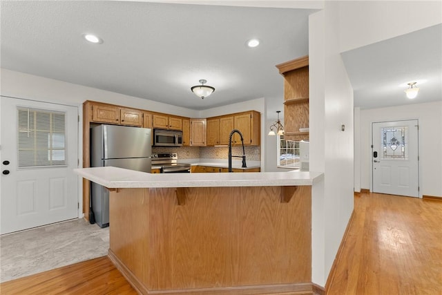 kitchen featuring light hardwood / wood-style floors, kitchen peninsula, appliances with stainless steel finishes, decorative backsplash, and a kitchen breakfast bar