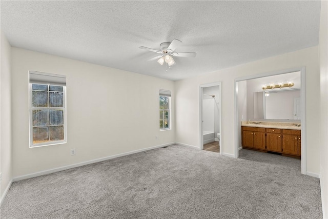 unfurnished bedroom featuring a textured ceiling, connected bathroom, sink, ceiling fan, and light colored carpet