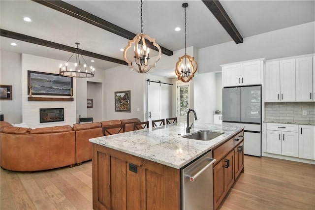 kitchen with a barn door, dishwasher, a center island with sink, sink, and white cabinets