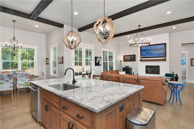 kitchen with a fireplace, sink, hanging light fixtures, an island with sink, and french doors