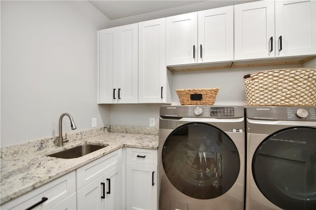 clothes washing area featuring sink, washing machine and clothes dryer, and cabinets