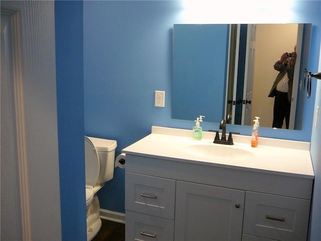 half bathroom with baseboards, toilet, and vanity