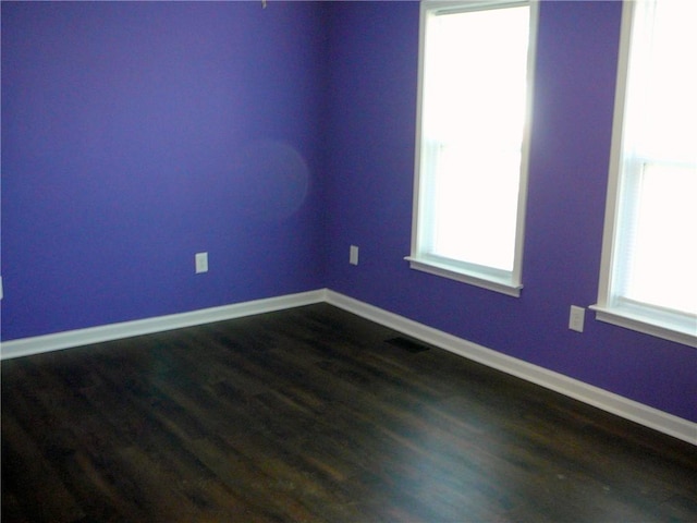 unfurnished room with a healthy amount of sunlight, dark wood-type flooring, and baseboards