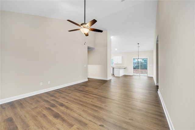 unfurnished living room featuring ceiling fan with notable chandelier, dark hardwood / wood-style flooring, and vaulted ceiling