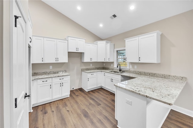 kitchen with kitchen peninsula, sink, white cabinetry, dark wood-type flooring, and light stone countertops