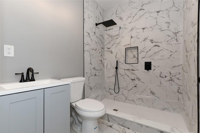 bathroom with toilet, a tile shower, and vanity