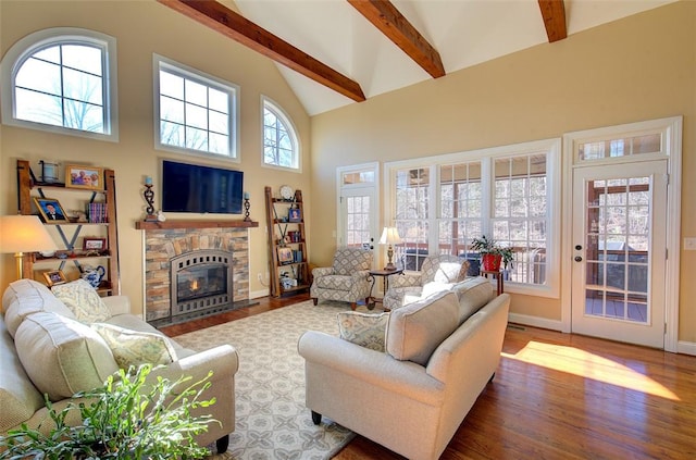 living room featuring a towering ceiling, wood-type flooring, a stone fireplace, and beamed ceiling