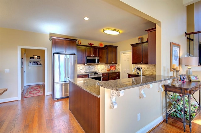 kitchen with backsplash, a breakfast bar, kitchen peninsula, light stone countertops, and appliances with stainless steel finishes