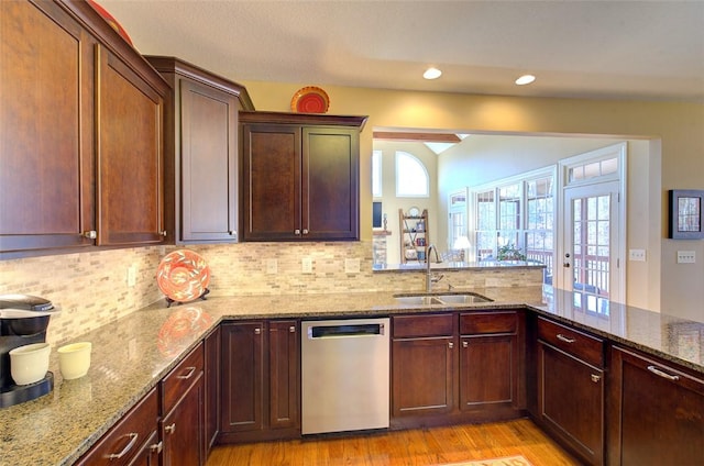 kitchen with stainless steel dishwasher, kitchen peninsula, decorative backsplash, sink, and light stone countertops