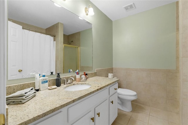 bathroom with tile patterned floors, vanity, a shower, tile walls, and toilet