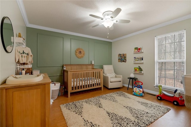 bedroom with ceiling fan, light hardwood / wood-style flooring, crown molding, and a crib