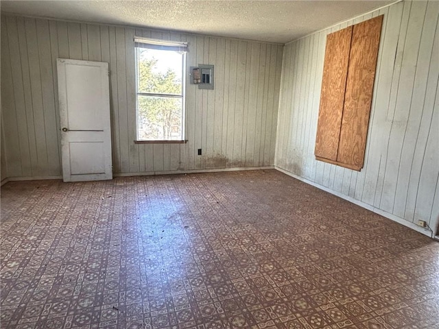 spare room featuring a textured ceiling, electric panel, and wood walls