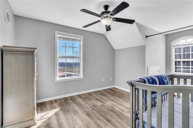 unfurnished bedroom with lofted ceiling, a crib, light hardwood / wood-style flooring, and ceiling fan