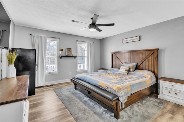 bedroom featuring ceiling fan, light hardwood / wood-style floors, and a textured ceiling