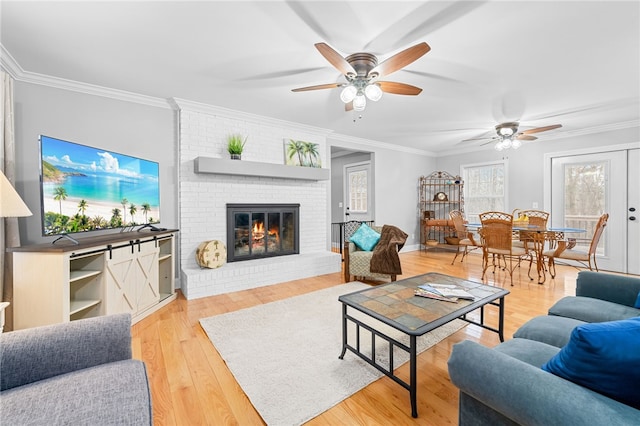 living room with crown molding, ceiling fan, a brick fireplace, and light hardwood / wood-style flooring