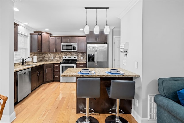 kitchen with appliances with stainless steel finishes, sink, a breakfast bar area, hanging light fixtures, and light hardwood / wood-style floors