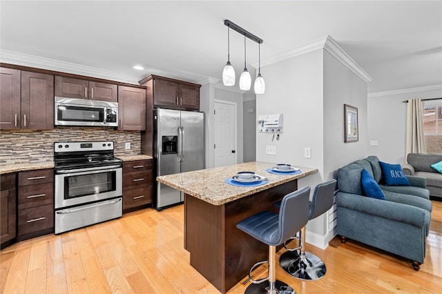 kitchen featuring appliances with stainless steel finishes, backsplash, hanging light fixtures, ornamental molding, and a kitchen bar