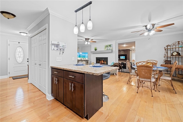 kitchen with a breakfast bar, a fireplace, decorative light fixtures, light hardwood / wood-style floors, and dark brown cabinetry