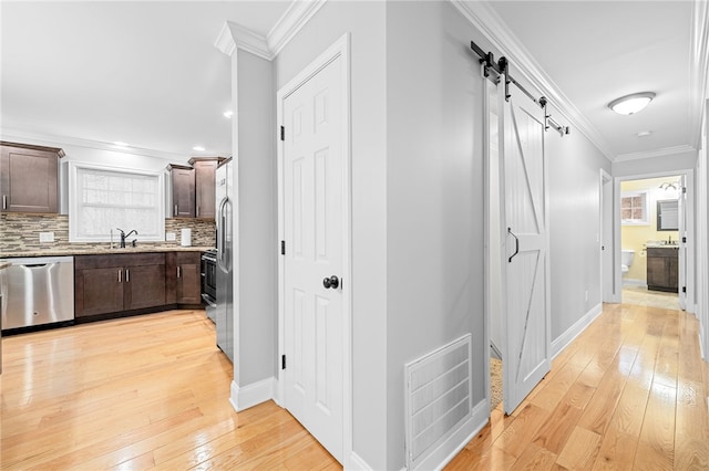 hallway with ornamental molding, a barn door, and light wood-type flooring