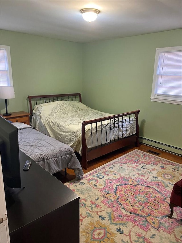 bedroom featuring hardwood / wood-style flooring, multiple windows, and a baseboard heating unit