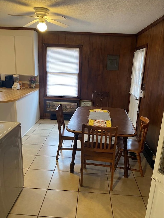 dining area with a textured ceiling, washer / dryer, wood walls, ceiling fan, and light tile patterned floors