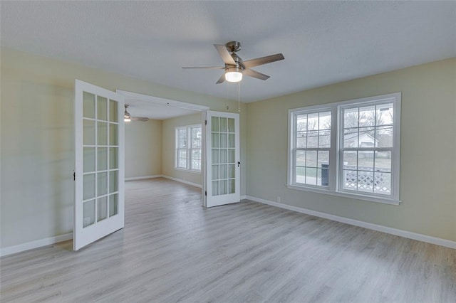 empty room with ceiling fan, a textured ceiling, light hardwood / wood-style flooring, and french doors